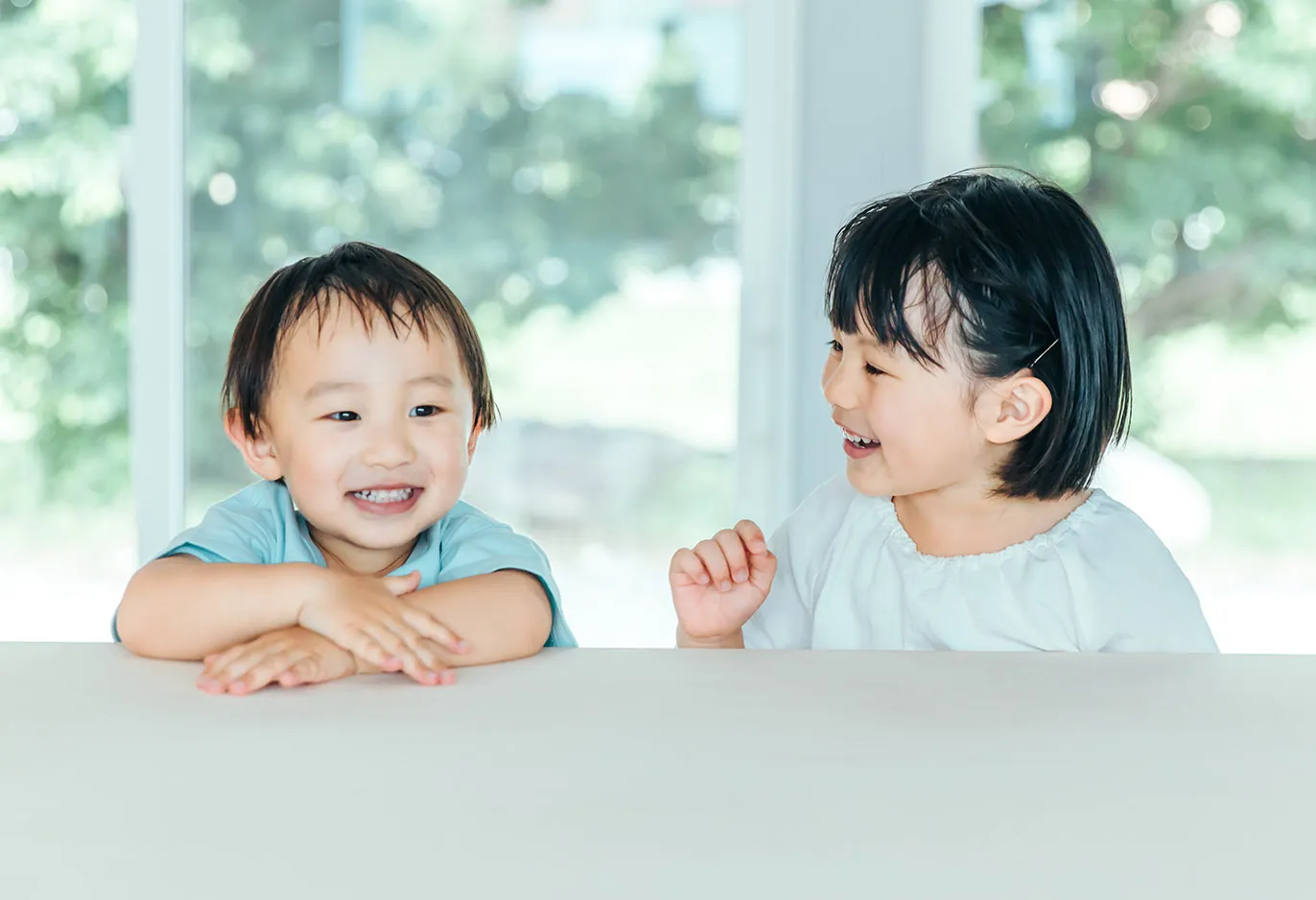保育室のテーブル越しに、二人の園児が笑い合っている