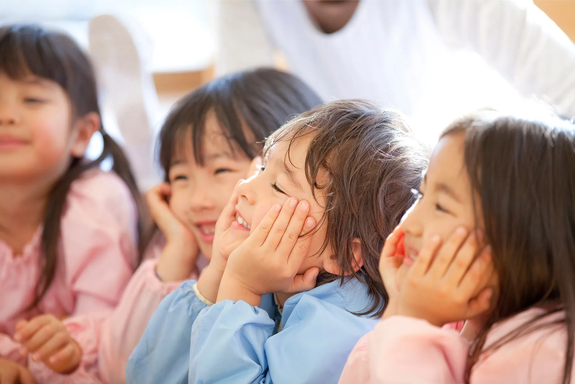 スモックを着た子どもたちが頬に手をあてて笑っている
